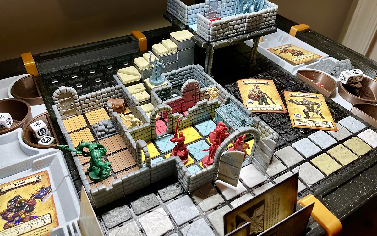 A quest on a StageTop table built from Dynamod tiles: rooms with wood, stone and blue floors, arched doors, a stair up to a raised room on pillars, and hero and monster miniatures